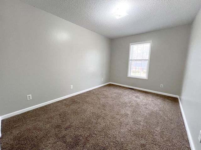 spare room featuring dark colored carpet, visible vents, a textured ceiling, and baseboards