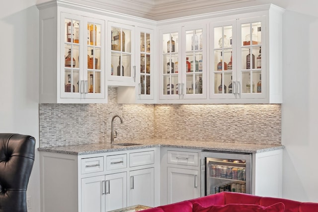 bar featuring backsplash, sink, light stone countertops, white cabinets, and beverage cooler