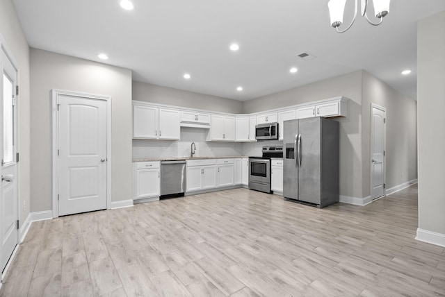 kitchen with decorative backsplash, stainless steel appliances, white cabinetry, and light hardwood / wood-style flooring