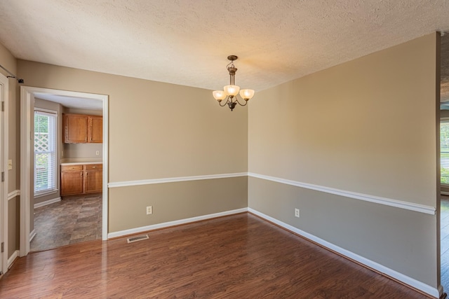 empty room with dark wood-type flooring, a textured ceiling, and an inviting chandelier