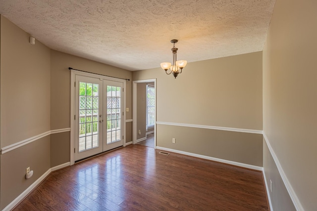 empty room featuring a textured ceiling, dark hardwood / wood-style floors, a chandelier, and french doors