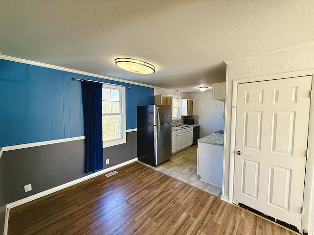 kitchen featuring crown molding, black dishwasher, light hardwood / wood-style floors, white cabinetry, and stainless steel refrigerator