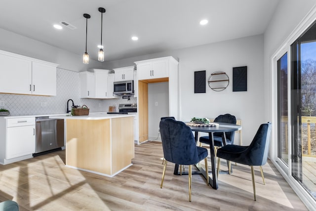 kitchen featuring white cabinets, appliances with stainless steel finishes, a center island, decorative light fixtures, and backsplash