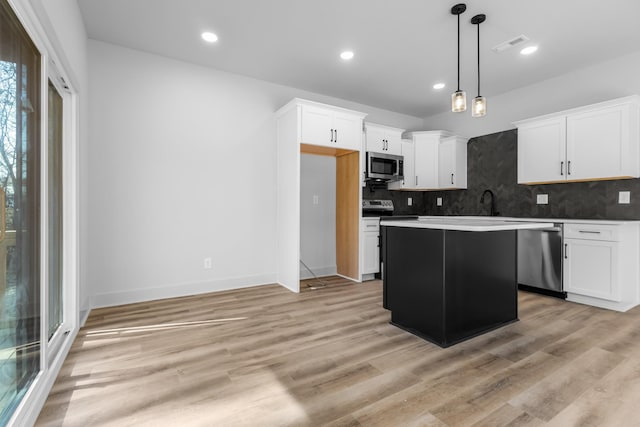 kitchen featuring stainless steel appliances, white cabinets, hanging light fixtures, and a center island