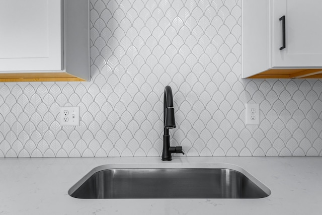 interior details with light stone counters, sink, backsplash, and white cabinets