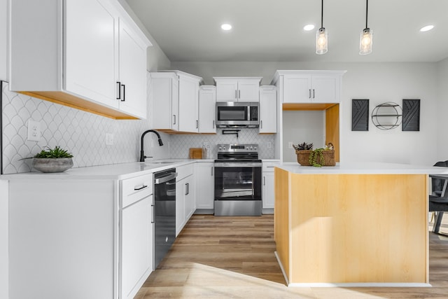 kitchen featuring appliances with stainless steel finishes, a kitchen breakfast bar, hanging light fixtures, white cabinets, and sink