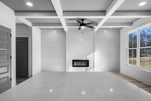 unfurnished living room featuring ceiling fan, coffered ceiling, wooden walls, and beamed ceiling