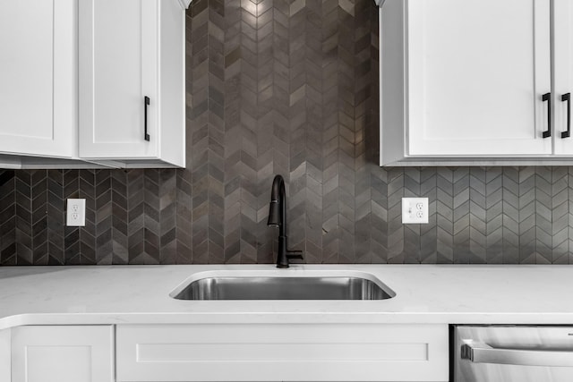 kitchen with tasteful backsplash, dishwasher, sink, white cabinets, and light stone counters