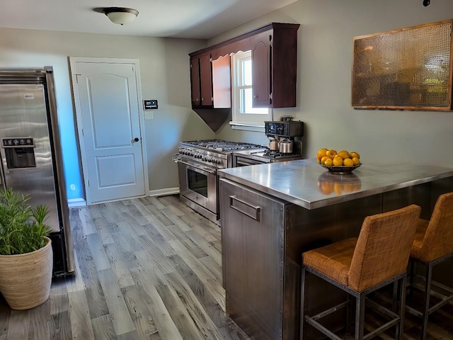 kitchen with a breakfast bar area, stainless steel counters, appliances with stainless steel finishes, light wood-style floors, and dark brown cabinets