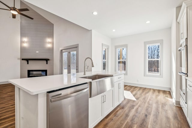 kitchen with appliances with stainless steel finishes, sink, a fireplace, white cabinetry, and an island with sink