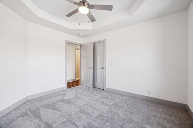 carpeted empty room with a raised ceiling and ceiling fan