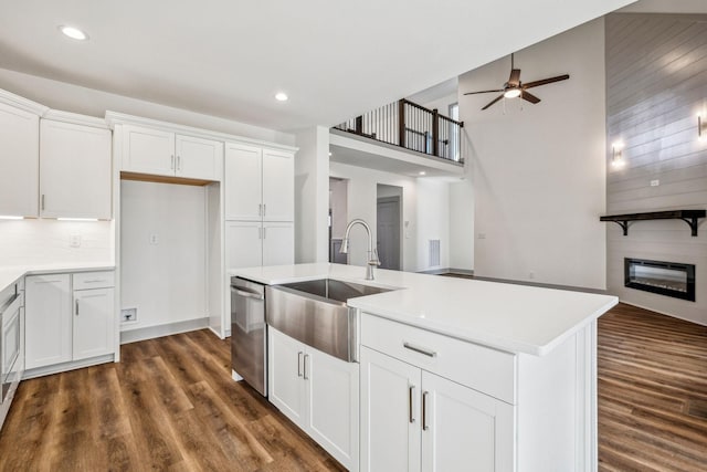 kitchen featuring stainless steel dishwasher, a fireplace, white cabinetry, and an island with sink