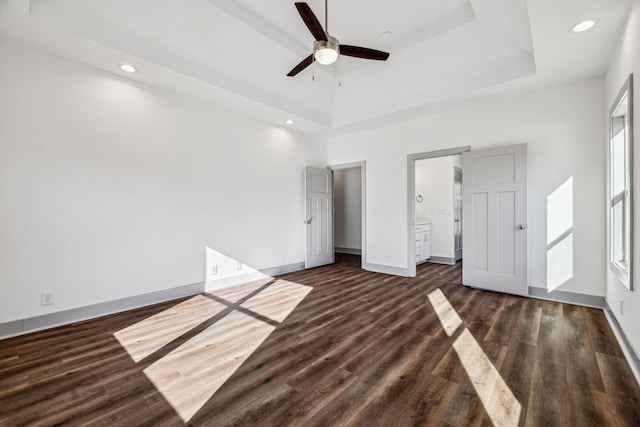 unfurnished bedroom featuring ensuite bathroom, a raised ceiling, ceiling fan, a high ceiling, and dark hardwood / wood-style floors