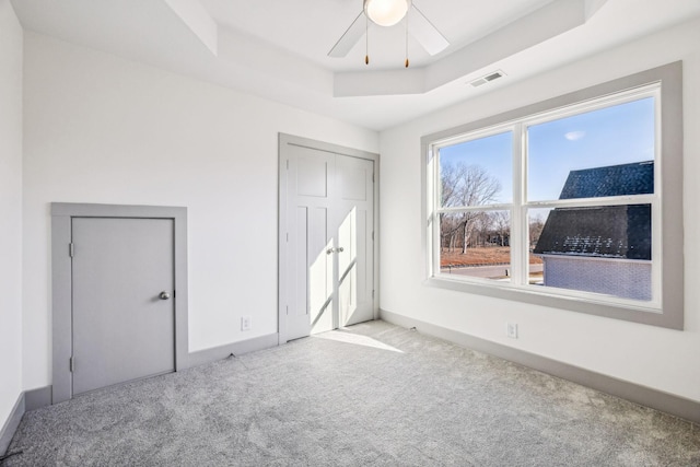 unfurnished bedroom featuring ceiling fan, a closet, light colored carpet, and a tray ceiling