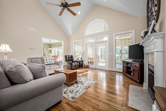 living room with a tile fireplace, ceiling fan with notable chandelier, a wealth of natural light, and high vaulted ceiling