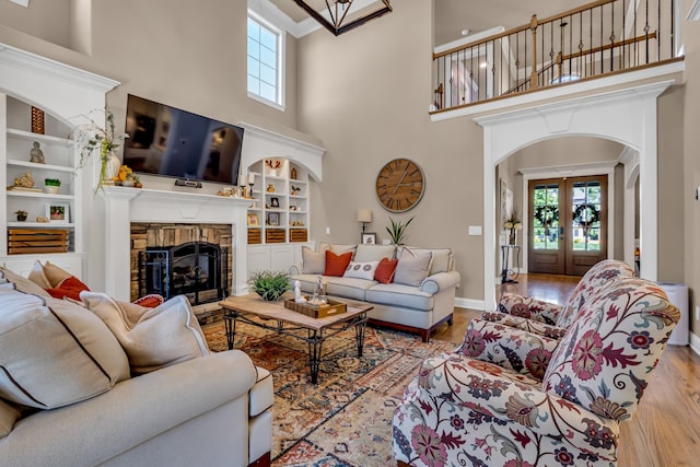 living room featuring french doors, light hardwood / wood-style flooring, built in features, and a stone fireplace