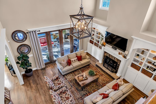 living room with french doors, a brick fireplace, a notable chandelier, a towering ceiling, and wood-type flooring