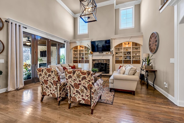 living room featuring french doors, a towering ceiling, crown molding, built in features, and hardwood / wood-style floors