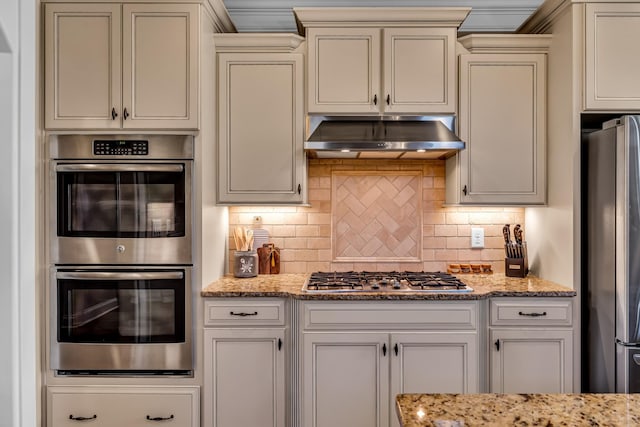 kitchen featuring tasteful backsplash, light stone counters, stainless steel appliances, crown molding, and exhaust hood