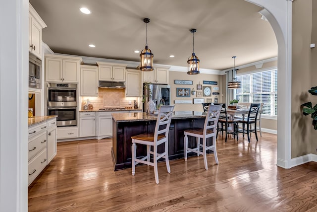 kitchen featuring pendant lighting, stainless steel appliances, light stone counters, and a kitchen island with sink