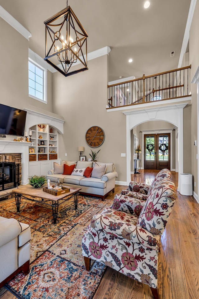 living room featuring an inviting chandelier, french doors, built in shelves, light wood-type flooring, and ornamental molding