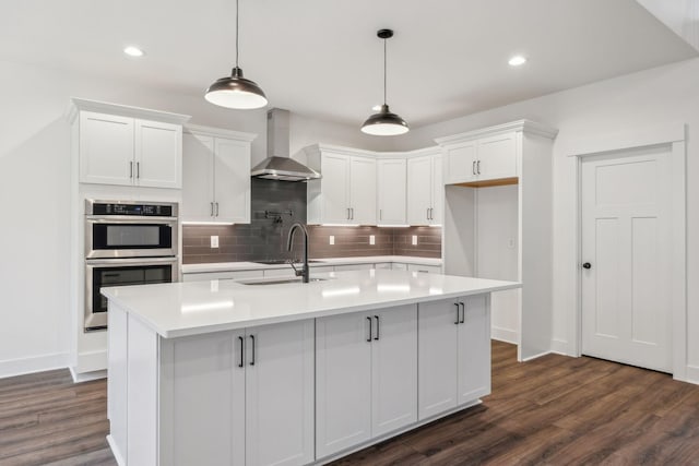 kitchen with wall chimney exhaust hood, white cabinetry, sink, and an island with sink