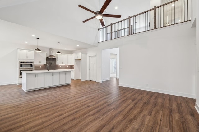 unfurnished living room featuring a towering ceiling, dark hardwood / wood-style floors, ceiling fan, and sink