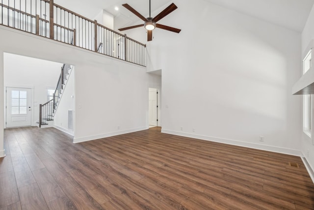 unfurnished living room featuring ceiling fan, dark hardwood / wood-style flooring, and a high ceiling