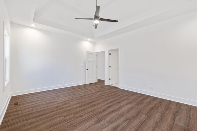 unfurnished room featuring ceiling fan, dark wood-type flooring, and a tray ceiling