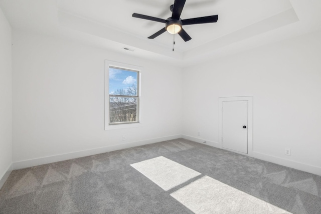 spare room with carpet, a tray ceiling, and ceiling fan