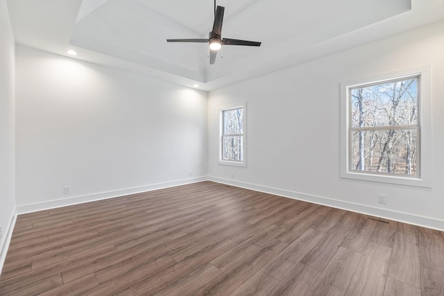 empty room featuring ceiling fan, dark hardwood / wood-style flooring, and a tray ceiling