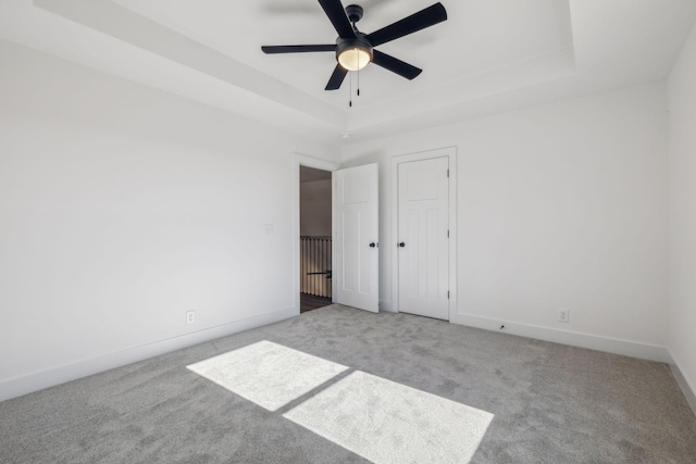 unfurnished bedroom featuring ceiling fan, light carpet, and a tray ceiling