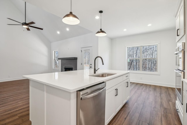 kitchen with white cabinetry, sink, stainless steel appliances, decorative light fixtures, and a center island with sink