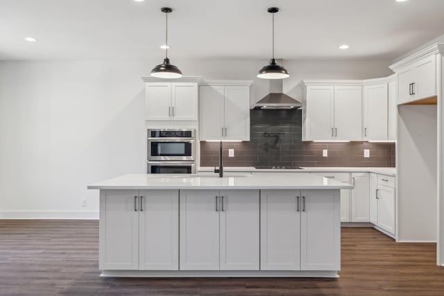 kitchen with white cabinetry, sink, wall chimney exhaust hood, an island with sink, and pendant lighting