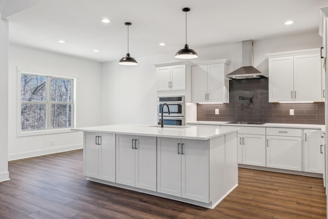 kitchen with a center island with sink, white cabinetry, and wall chimney range hood