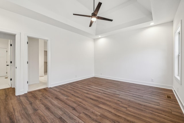 empty room with a tray ceiling, ceiling fan, and dark wood-type flooring