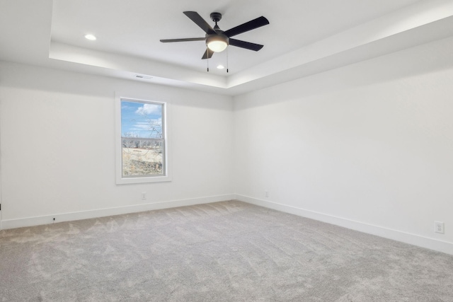 carpeted spare room featuring a tray ceiling and ceiling fan