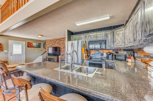 kitchen with sink, stainless steel appliances, kitchen peninsula, a textured ceiling, and a kitchen bar