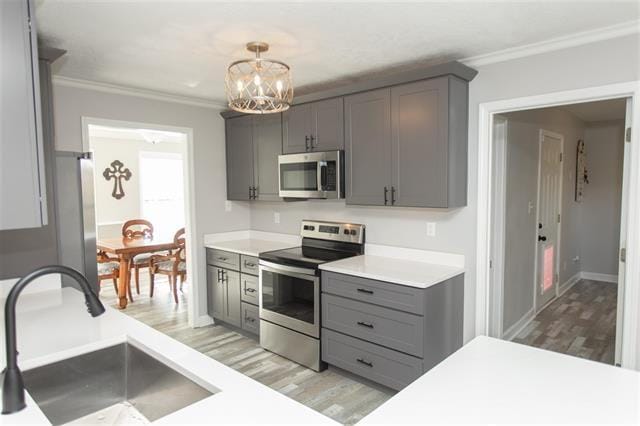 kitchen with ornamental molding, gray cabinetry, stainless steel appliances, sink, and decorative light fixtures