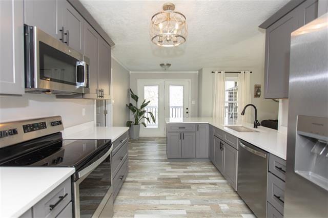 kitchen with gray cabinetry, sink, a notable chandelier, pendant lighting, and appliances with stainless steel finishes