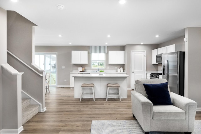 kitchen featuring appliances with stainless steel finishes, a breakfast bar, a kitchen island, light hardwood / wood-style floors, and white cabinetry