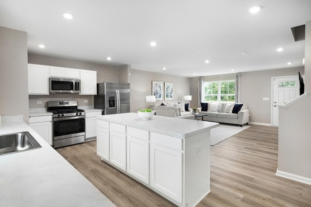 kitchen with white cabinets, appliances with stainless steel finishes, light hardwood / wood-style flooring, and a kitchen island