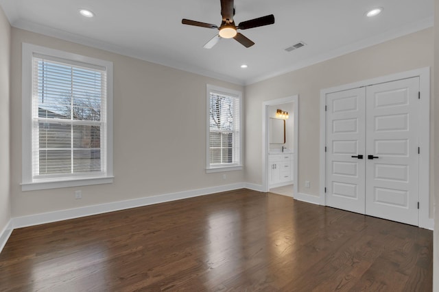 unfurnished bedroom featuring ceiling fan, ensuite bath, dark wood-type flooring, ornamental molding, and a closet