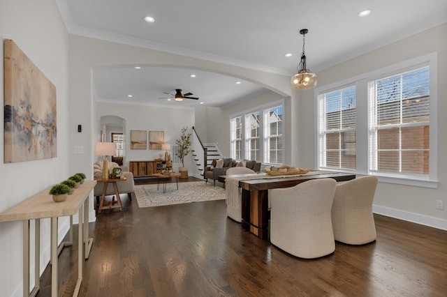 living room featuring dark wood-type flooring, ornamental molding, and ceiling fan with notable chandelier