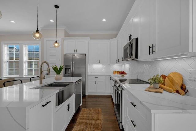 kitchen with hanging light fixtures, backsplash, appliances with stainless steel finishes, and a center island with sink