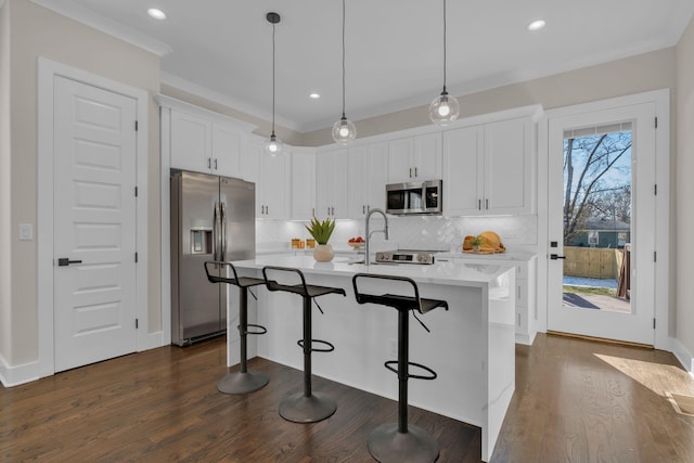 kitchen featuring white cabinetry, stainless steel appliances, tasteful backsplash, a kitchen island with sink, and hanging light fixtures