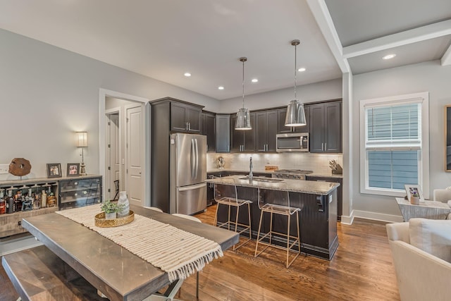 kitchen featuring light stone countertops, hanging light fixtures, a kitchen breakfast bar, a kitchen island with sink, and appliances with stainless steel finishes