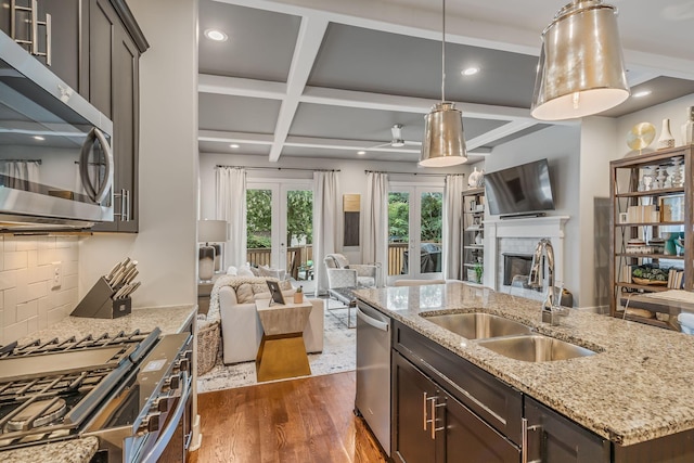 kitchen with appliances with stainless steel finishes, french doors, coffered ceiling, a kitchen island with sink, and sink