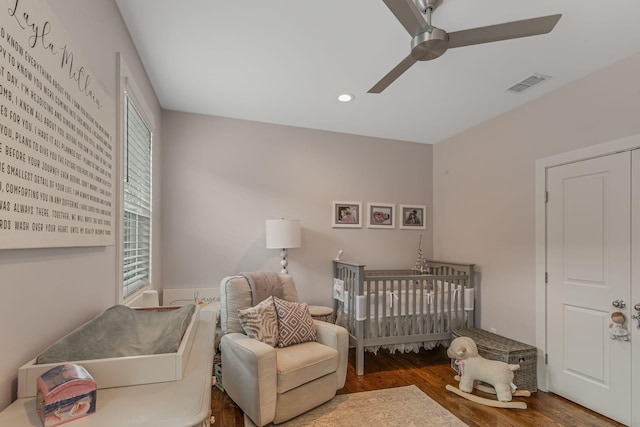 bedroom featuring dark hardwood / wood-style flooring, a nursery area, and ceiling fan