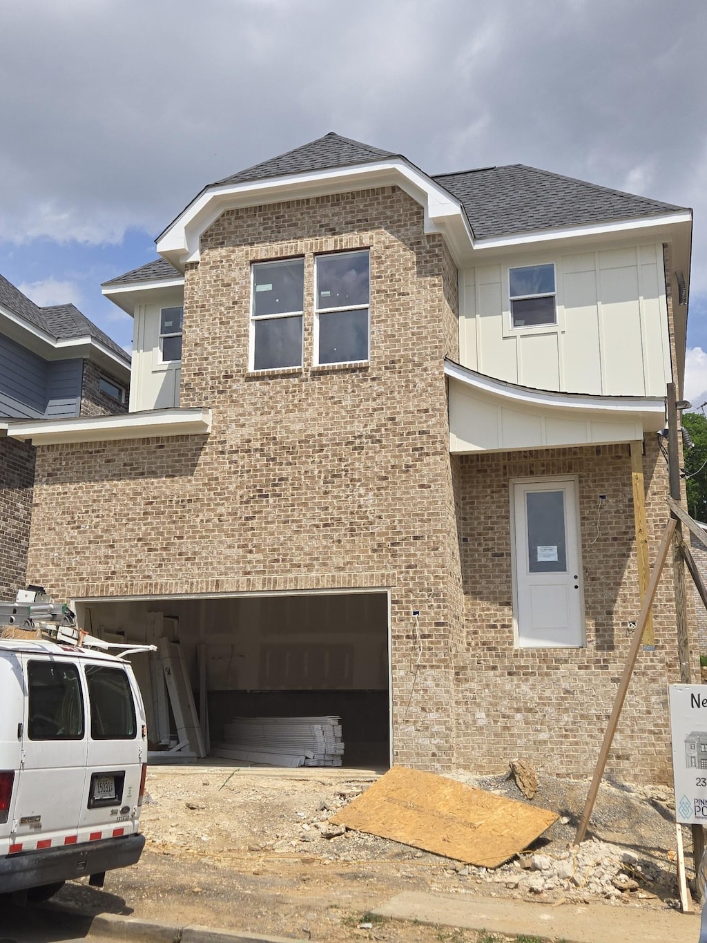 view of front facade featuring roof with shingles, an attached garage, brick siding, dirt driveway, and board and batten siding